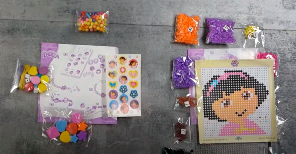 Deux kits d’activités Dora avec perles, stickers et modèles sur carrelage gris