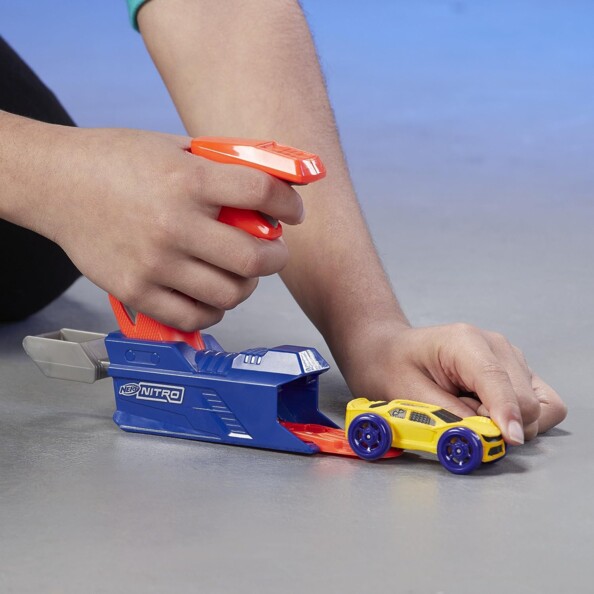Enfant tenant le manche du lanceur bleu et orange le doigt sur la gâchette tandis qu'il charge une voiture jaune et bleue dans la plateforme de lancement