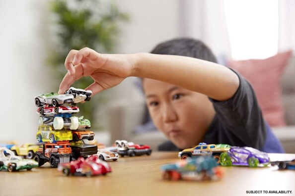 Petit enfant asiatique empilant des petits véhicules colorés les uns sur les autres sous forme de tour sur une table de salle à manger
