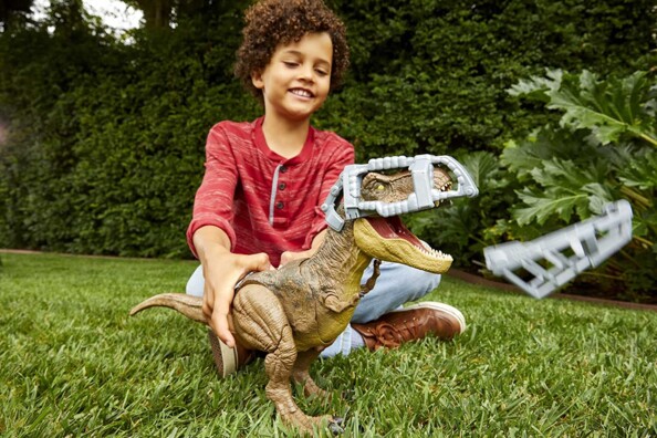 Enfant métisse jouant dans le jardin avec la figure T-Rex Mattel, la cage de protection de la mâchoire du dinosaure étant éjectée d'une pression sur le bouton prévu à cet effet