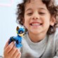 Jeune garçon châtain frisé avec pull gris tenant dans sa main la figurine articulée du chien de la Pat' Patrouille Chase en tenue de super héros