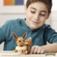 Jeune garçon souriant en sweatshirt bleu canard entrain de jouer avec la figurine en briques de construction type Lego Pokémon Evoli
